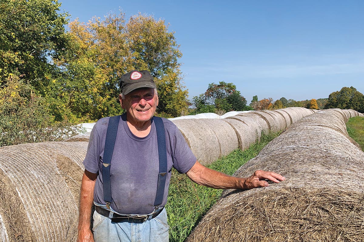 Albert standing next to a field of rolled hale bales